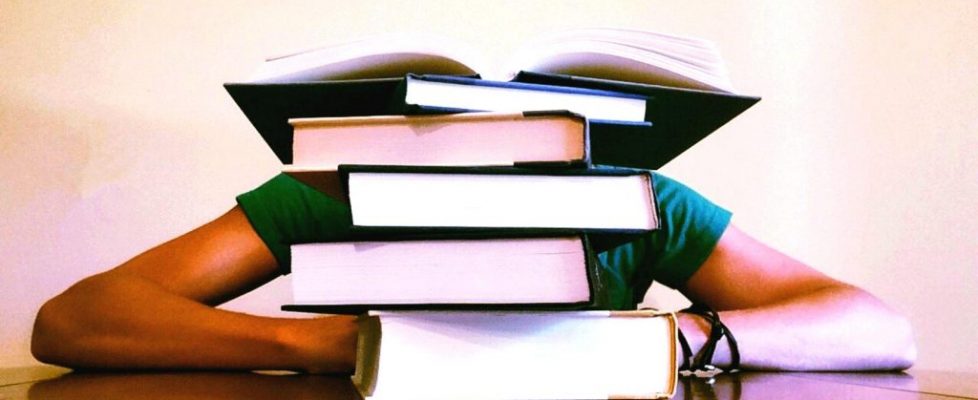man-sitting-behind-pile-of-books-boost